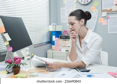 Serious Businesswoman At Office Desk Reading A Financial Newspaper.