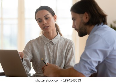 Serious businesswoman team leader explaining project to new employee, using laptop, pointing at screen, business coach mentor training intern, business team discussing strategy, working together