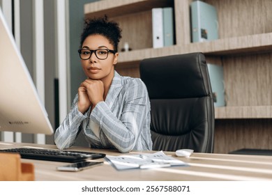 Serious businesswoman wearing stylish eyeglasses is sitting at her desk with her hands clasped, exuding confidence and professionalism in a contemporary office setting. Business concept - Powered by Shutterstock