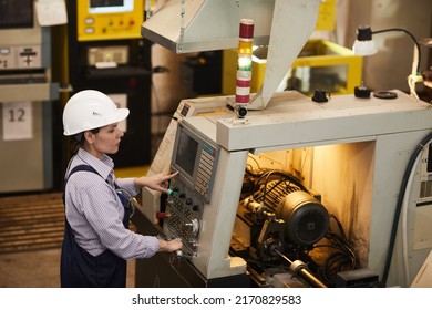 Serious busy female technical engineer standing at cnc lathe and pushing buttons while choosing Cnc machining operations at factory