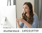 Serious call center operator in wireless headset talking with customer, woman in headphones with microphone consulting client on phone in customer support service, looking at computer screen close up