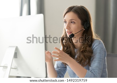 Serious call center operator in wireless headset talking with customer, woman in headphones with microphone consulting client on phone in customer support service, looking at computer screen close up