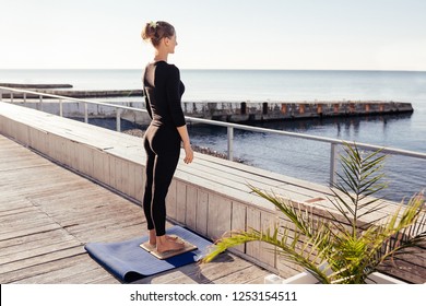 Serious Calm Attractive Young Woman In Sports Clothing Keeping Eyes Closed And Meditating While Preparing For Standing On Board With Sharp Nails Outdoor Against The Sea On Wooden Fitnes Terrace