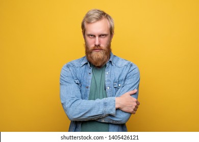 Serious and calm young hipster look scowl on camera. Angry and mad. Hands crossed. Wear jeans jacket and green shirt. Isolated alone on yellow background - Shutterstock ID 1405426121
