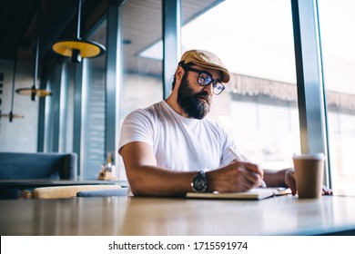 Serious caucasian bearded male author in eyewear for vision correction writing in notepad working on freelance in cafe interior, pensive mature man making notes of ideas and plans during free time - Powered by Shutterstock