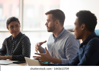 Serious caucasian business man manager talk meeting indian african people work group sit at conference table, diverse team listen to coach mentor boss consult clients at corporate office briefing