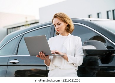 Serious caucasian businessman using laptop computer working online standing near car