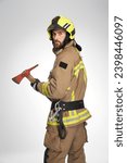 Serious caucasian firefighter in helmet holding big axe in studio. View from shoulder of bearded male rescuer with hatchet, looking at camera, on gray background. Concept of job, fireman equipment.