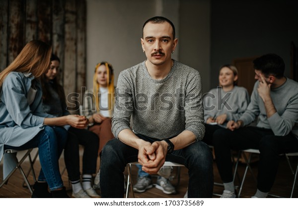 serious
caucasian man, member of alcoholics anonymous club sit in center of
isolated room. people support each other in the background, sit in
the circle. help, support, problem,
psychotherapy