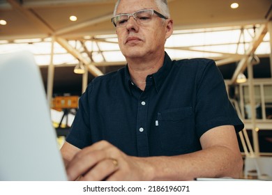 Serious Caucasian Mature Male Executive Wearing Eyeglasses Doing Research Over Laptop While Working In Corporate Office