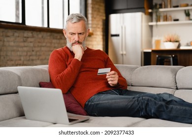 Serious caucasian mature middle-aged man doing shopping online, buying purchasing presents clothes remotely, ordering food delivery with credit card e-commerce banking on laptop at home