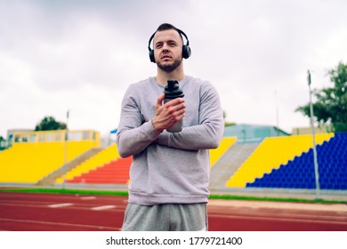 Serious Caucasian Sportsman Listening Audiobook Via Modern Stereo Sound Accessory Making Break On Workout, Handsome Hipster Guy Jogger Making Break For Drinking Water Enjoying Playlist In Headphones