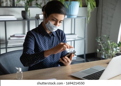 Serious Cautious Young Indian Ethnicity Woman Wearing Breath Protective Medical Mask, Cleaning Mobile Phone Screen With Antibacterial Napkin, Preventing Spreading Coronavirus Infection At Home Office.