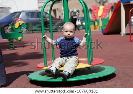 Serious child is sitting on roundabout in summer