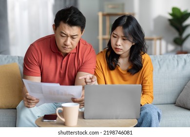 Serious Chinese Couple Paying Bills Online While Staying Home, Sitting On Couch, Using Laptop, Concentrated Chinese Man And Woman Checking Papers And Banking On Internet, Copy Space