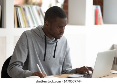 Serious Concentrated African American Male Student Using Laptop, Busy With Studying, Preparing For Evaluation Examination, Final Test Or Session. Motivated Black Guy Doing Homework Or Writing Essay.