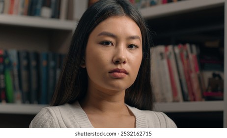 Serious concentrated asian woman girl student teenager businesswoman business lady teacher customer nod head approve agree looking at camera with piercing stern gaze posing indoors near bookshelf - Powered by Shutterstock