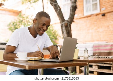 Serious, concentrated and enthusiastic african afro american man using laptop and drinking coffee in street internet cafe with wireless technology. Learning and preparing annual report, doing business
