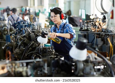 Serious concentrated lady engineer in ear protectors and protective goggles pouring lubricant for machine while working at factory - Powered by Shutterstock