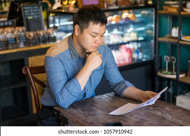 Serious Concentrated Man Choosing Lunch In Cafe And Learning Special Offers. Busy Coffee Shop Owner Working With Papers. Cozy Public Place Concept