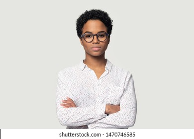 Serious Concentrated Young African American Girl In Eyeglasses Standing With Folded Hands, Headshot Studio Portrait. Focused Black Female Professional Looking At Camera, Isolated On Grey Background.