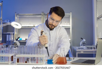 Serious Concentrated Young Male Medical Scientist, Pharma Chemist, Biotech Company Employee, Lab Assistant Or Student In Coat And Goggles Working Alone In Science Laboratory Late In The Evening