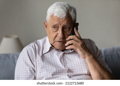 Serious concerned old grandpa talking on mobile phone, calling for emergency, ambulance. Senior 80s man speaking on cellphone, sitting on couch, at home, contact family on distance
