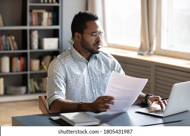 Serious confident African American man wearing glasses using laptop, holding document, paperwork, focused businessman accountant working on financial report, student writing research work - Shutterstock ID 1805431987