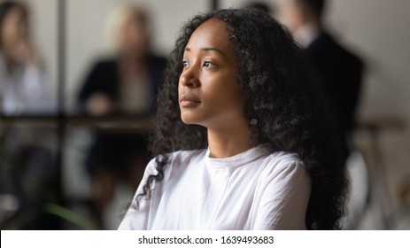 Serious confident african businesswoman standing in shared office look out the window planning future project, thinking search solution lost in thoughts. Successful businesswoman company owner concept