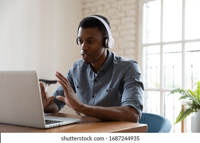 Serious confident African manager wear headphones looking at laptop screen talking provide support to client distantly, convincing customer buy company services. Student and e-learning process concept