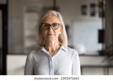 Serious confident blonde senior businesswoman in elegant eyeglasses and formal shirt posing in office, looking at camera. Female professional, business leader woman front portrait - Powered by Shutterstock