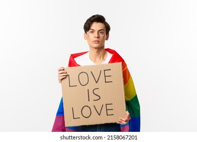 Serious And Confident Gay Man Wearing Rainbow Lgbt Flag, Holding Sign For Pride Parade, Standing Over White Background