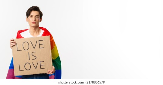 Serious And Confident Gay Man Wearing Rainbow Lgbt Flag, Holding Sign For Pride Parade, Standing Over White Background