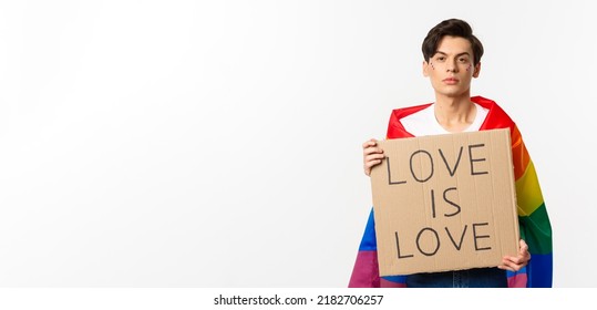 Serious And Confident Gay Man Wearing Rainbow Lgbt Flag, Holding Sign For Pride Parade, Standing Over White Background