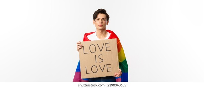 Serious And Confident Gay Man Wearing Rainbow Lgbt Flag, Holding Sign For Pride Parade, Standing Over White Background