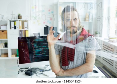 Serious Confident Handsome Young Computer Programmer With Beard Developing Code For Software And Holding Felt Tip Pen While Looking At Data In Glassy Board In Office.