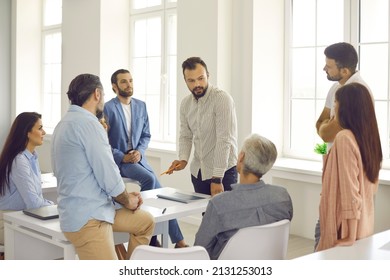 Serious confident male manager or coach speaking at corporate business group meeting. Man explains new idea and instructs by talking to office workers during training. Business education concept. - Shutterstock ID 2131253013