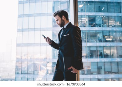 Serious Confident Male Manager In Suit Holding Mobile Phone Checking Notification About Income Mail Near Panoramic Windows In Office, Confident Businessman Read Information From Web Page On Cellular