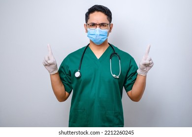 Serious And Confident Male Nurse In Green Scrubs, Medical Mask, Pointing Fingers Up, Inform Patients How Prevent Corona Infection Standing Over White Background