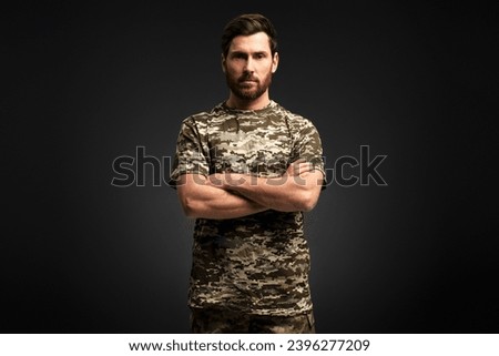 Serious confident soldier, veteran  holding arms crossed wearing military camouflage uniform looking at camera isolated on black background