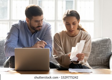 Serious Couple Calculating Expenses, Bills Together, Using Laptop, Sitting On Couch At Home, Checking Documents, Confused Man And Woman Planning Budget, Discussing Loan Or Debt Problem