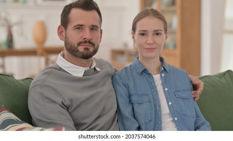 Serious Couple Looking At The Camera While Sitting On Sofa