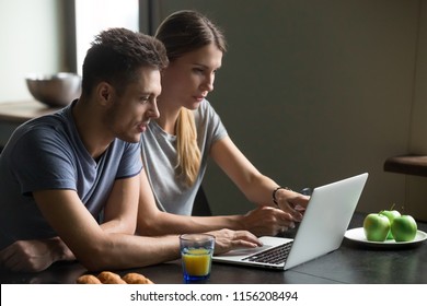 Serious couple using laptop for reading and discussing morning news or online work having breakfast at home, young family talking making plans searching information in internet on computer together