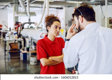 Serious cute caucasian female employee standing with arms crossed and listening angry director. Printing shop interior.