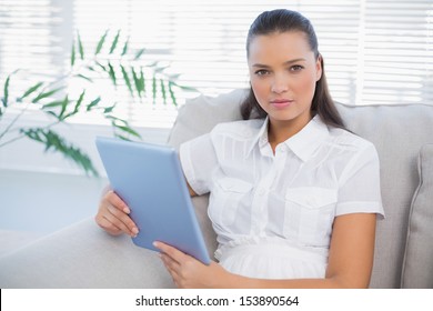 Serious Cute Woman Holding Tablet Sitting On Cosy Sofa In Bright Living Room