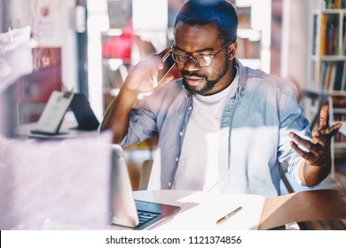 Serious Dark Skinned Male Making Telephone Call To Customer Support Service Upset With Bad Wireless Connection In Office, Angry African American Freelancer Gesturing During Mobile Phone Conversation