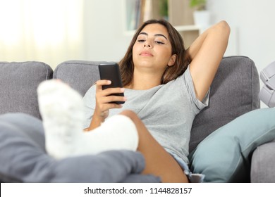 Serious Disabled Woman Using A Smart Phone Sitting On A Couch In The Living Room At Home