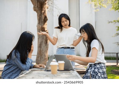 A serious, disappointed young Asian female student is expressing concerns about project issues while brainstorming at a table in their college park, having a serious conversation. - Powered by Shutterstock