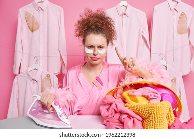 Serious Displeased Femae Housekeeper Looks Angrily At Camera Raises Index Finger Asks To Wait One Minute Finished Ironing Laundry Applies Pads Under Eyes To Reduce Wrinkes Wears Dressing Gown