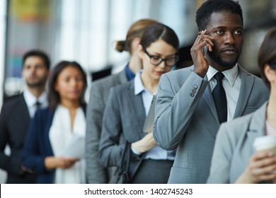 Serious Displeased Young African-American Businessman With Beard Standing In Line And Calling On Mobile Phone While Waiting For Business Forum Registration